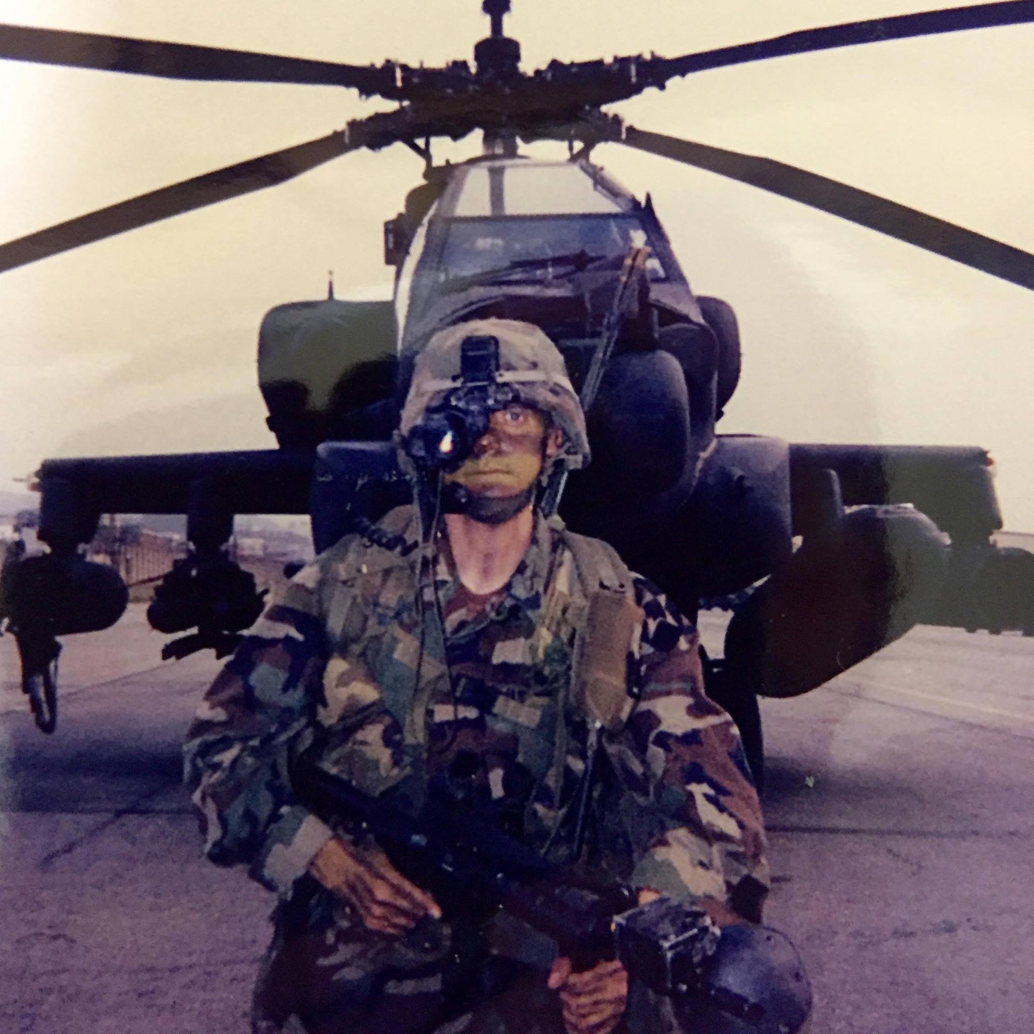 Barrett McNabb wearing night vision equipment in front of a military helicopter